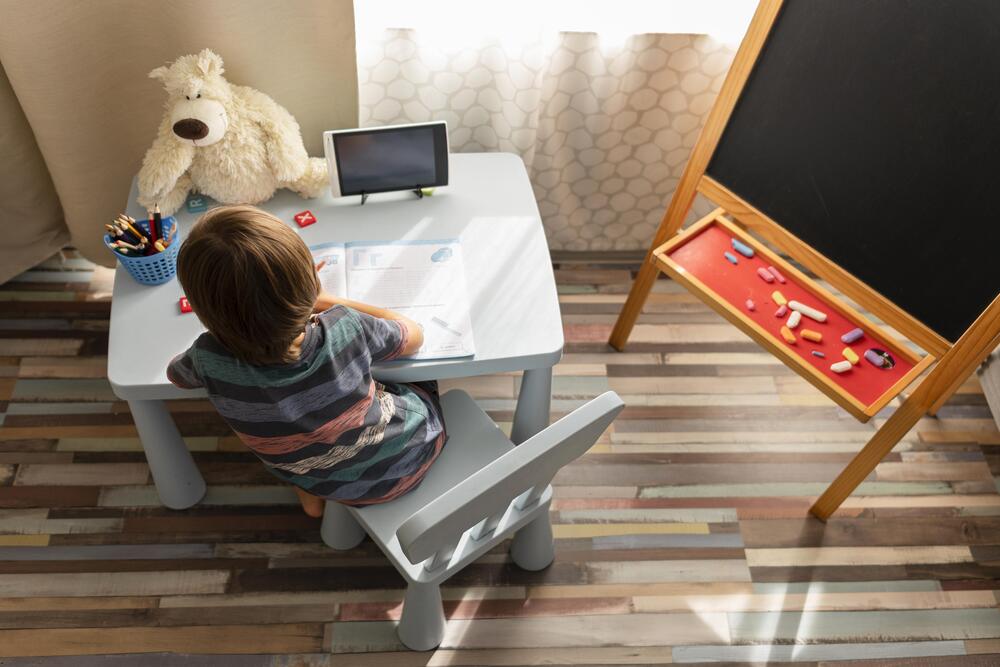 Niño estudiando en una mesa infantil con una pizarra y materiales de escritura, resaltando la importancia de un espacio adecuado para el desarrollo y la autonomía infantil.